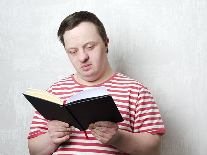 A young man wearing a red striped shirt reads a book.