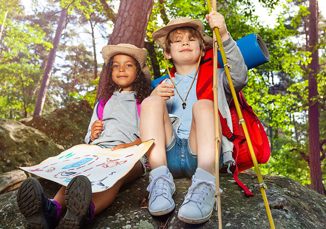 A girl a boy sit on a rock holding a map.  